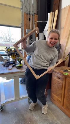 a woman standing in front of a table holding up a wooden frame that has been cut into