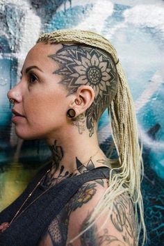 a woman with tattoos on her face and neck is standing in front of a painting