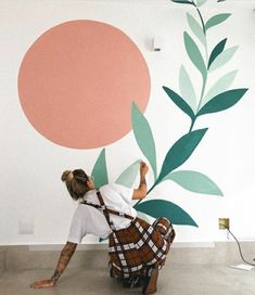 a woman is painting a mural on the wall with green leaves and orange circles behind her