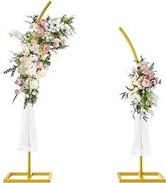 two tall vases with flowers are on stands