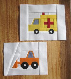 two pieces of paper are cut out to look like construction vehicles on white fabric, sitting on a wooden surface