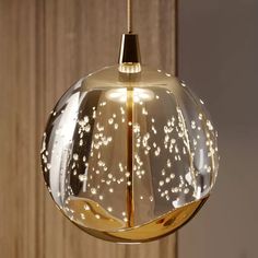 a glass light fixture hanging from a wooden wall with white dots on the bottom and gold trim