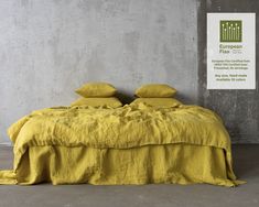 a bed with yellow linens and pillows in a concrete room next to a sign