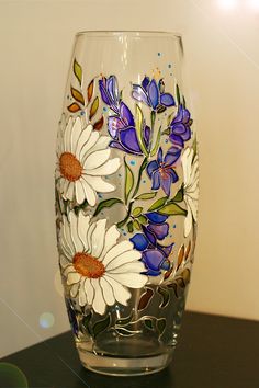 a glass with flowers painted on it sitting on a table