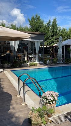 an empty swimming pool surrounded by umbrellas and tables with flowers in the foreground