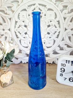 a blue vase sitting on top of a wooden table next to a clock and flowers