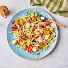 a blue plate topped with a salad next to a fork and knife on top of a table