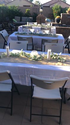 the table is set with white flowers and greenery for an outdoor party or gathering