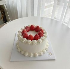 a white cake topped with raspberries sitting on top of a table next to a window