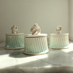 three white ceramic containers sitting on top of a counter next to a window sill