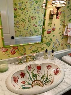 a bathroom sink sitting under a mirror in front of a green wallpapered wall