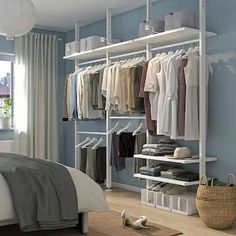 a bedroom with blue walls and white shelves filled with clothes on hangers next to a bed