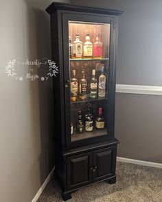 a cabinet with liquor bottles in it sitting on the floor next to a wall and carpet