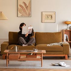 a person sitting on a couch reading a book in a living room with a coffee table