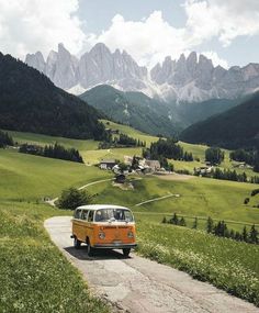 an orange and white vw bus driving down a road in front of some mountains