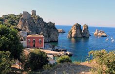 an old red building sitting on top of a cliff next to the ocean with boats in it