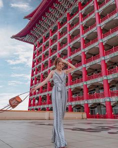 a woman standing in front of a tall building with red and white columns on it