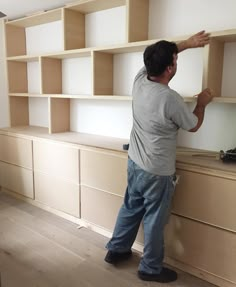 a man standing on top of a wooden shelf next to a wall filled with shelves