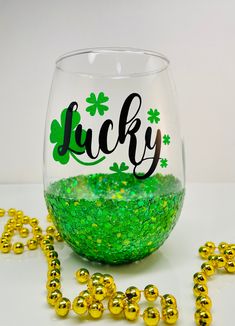 a glass filled with green liquid next to gold beads and shamrocks on the ground