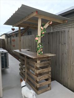 a dog standing in front of a wooden structure with flowers on it's roof