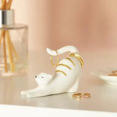 a white cat figurine sitting on top of a table next to some gold rings