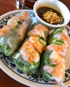 several rolls on a plate with dipping sauce next to it and a bowl of rice