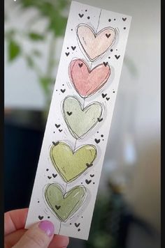 a hand holding up a piece of paper with hearts drawn on it in different colors