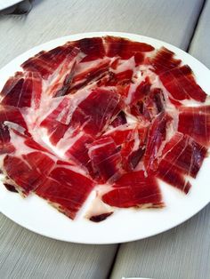 a white plate topped with sliced meat on top of a table