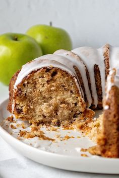 there is a piece of cake with icing on the plate next to two green apples