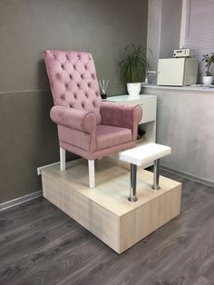 a pink chair sitting on top of a wooden platform next to a white table and potted plant