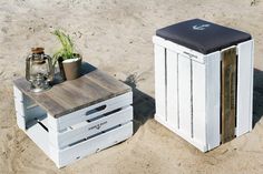 two wooden crates sitting on top of a sandy beach next to a potted plant