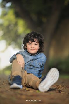 a little boy sitting on the ground with his legs crossed and smiling at the camera