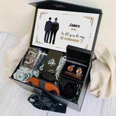 an open gift box containing two men's groomsmen items and a card