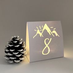 a pine cone sitting next to a card with the letter s on it and an image of mountains