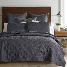 a bed with grey comforter and pillows in a room next to a lamp on a wooden headboard