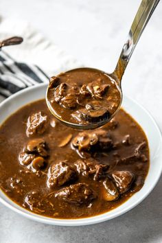 a spoon full of meat and mushrooms in gravy on top of a white plate