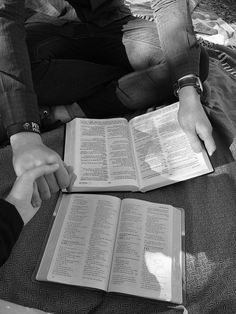 two people sitting on the ground with open books in their hands and one person pointing at them