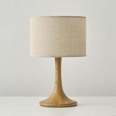 a wooden table lamp with a beige shade on it's side and a white wall in the background