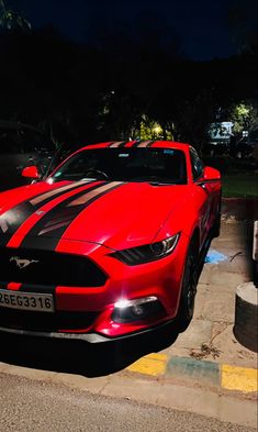 a red sports car parked on the side of the road at night with its lights on