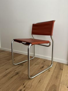 a red chair sitting on top of a hard wood floor next to a white wall