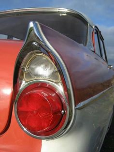 the rear end of an old red and white car with its tail light turned on