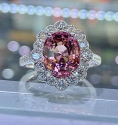 a fancy ring with an oval cut pink diamond surrounded by smaller round diamonds and white gold