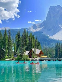 two canoes are on the water in front of a mountain lake with a dock