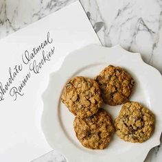 three cookies on a white plate next to a card and envelope that says, bake oatmeal brownies