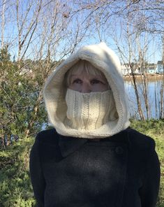 a woman wearing a white knitted hood and scarf over her face with trees in the background