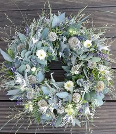 a wreath with white flowers and greenery on a wooden surface, ready to be hung