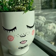 a potted plant with eyelashes painted on it sitting on a window sill next to a window