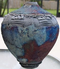 a blue and red vase sitting on top of a glass table next to a fence