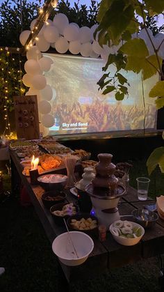 an outdoor movie screen is set up with food and drinks on the table in front of it