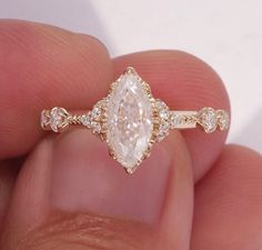 a close up of a person's hand holding a ring with an oval shaped diamond